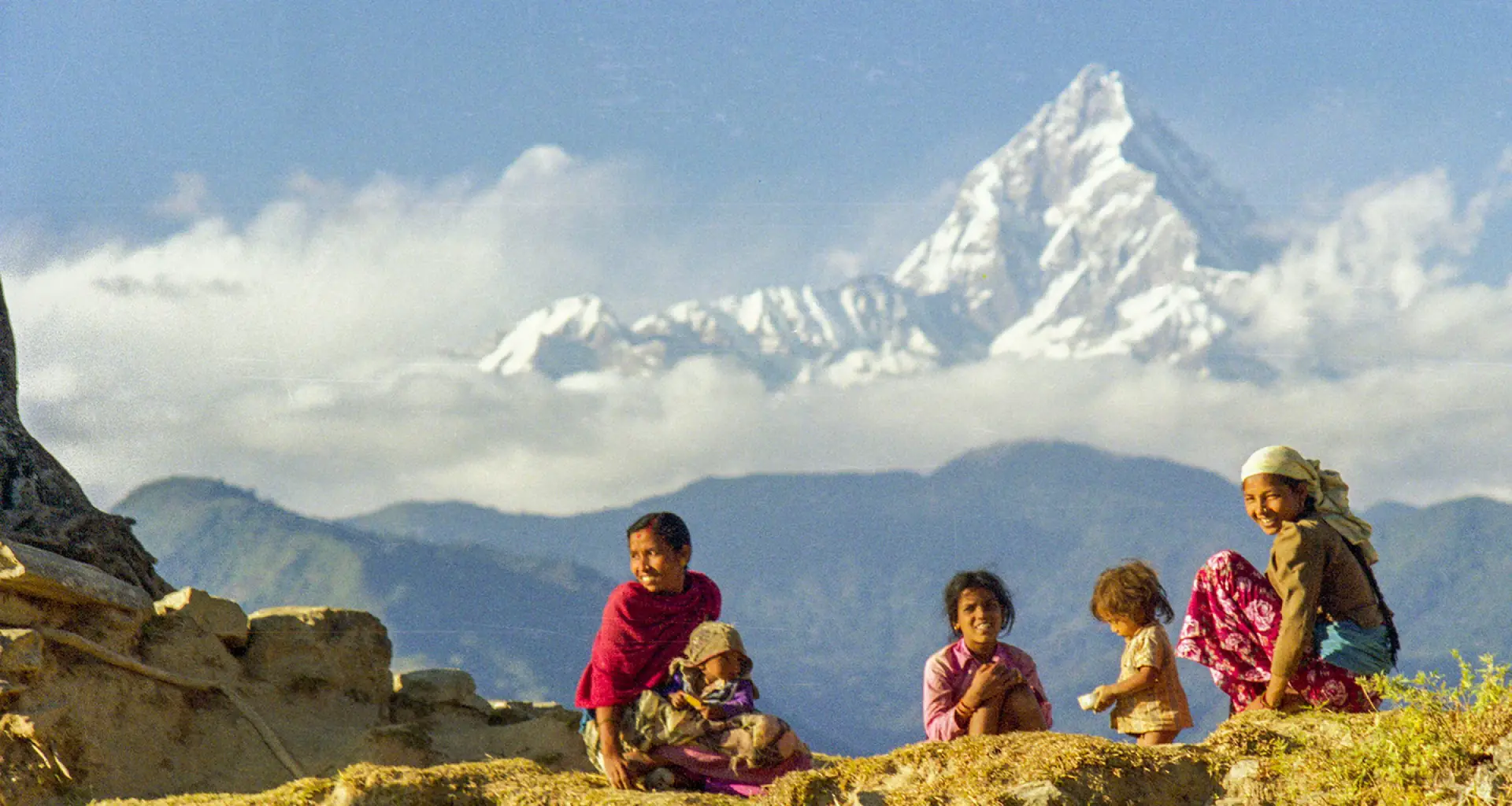 A mother and children resting on a ridge with a snow peak rising above the clouds behind them.